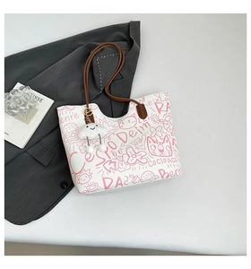 Dettaglio della borsa tote bianca con scarabocchi rosa, manici marroni e charm a nuvola