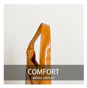 Detail view of the wide, glossy caramel leather shoulder strap on a handbag