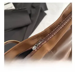 Detailed close-up of smooth metal zipper and leather texture on a brown tote bag