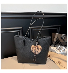 Detail of black lychee leather tote bag featuring a leopard print faux fur heart charm