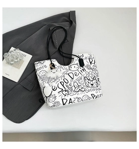 Dettaglio di una borsa tote bianca con graffiti e ciondolo a nuvola su blazer
