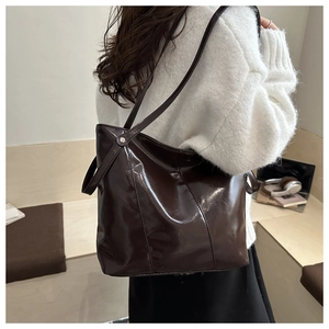Detail of dark coffee gloss leather tote bag with silver rivets and sleek shoulder strap
