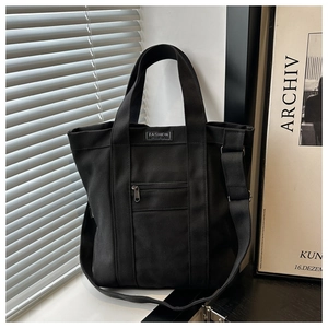 Détail du sac cabas en toile noire montrant la poche zippée et la bandoulière réglable