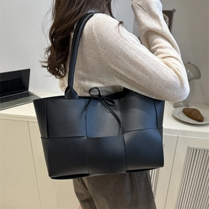 Large black woven tote bag made of synthetic leather worn by model in office setting