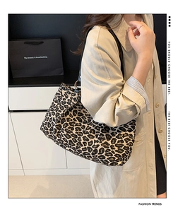 Detail of leopard print tote bag with black leather straps worn over a trench coat