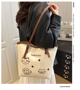 Close-up of a large beige tote bag with brown straps and cute cat illustration detail
