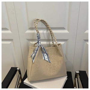 Detail of apricot tote bag with woven handles and decorative printed silk scarf charm