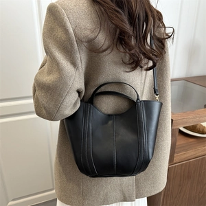 Minimalist black leather bucket bag set with twin handles and crossbody strap on model