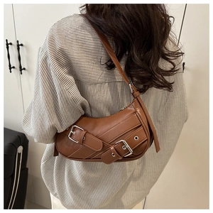 Detail of a brown leather crescent shoulder bag with punk buckles and silver eyelets