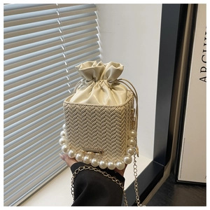 Detail of off-white woven bucket bag featuring large pearl handle and gold chain strap