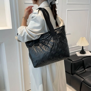 Black quilted puffer tote bag with 3D pattern and wide strap shown in a modern interior