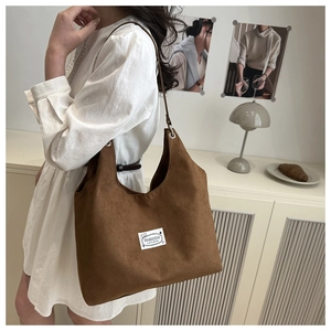 Brown suede hobo tote bag with fashion logo label carried by model in minimal setting