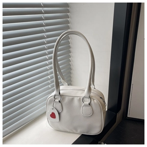 Close-up of white pebble-grain leather bag with silver rings and heart charm detail