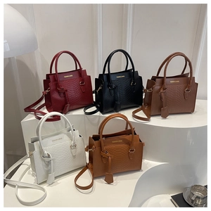 Close-up of five textured faux leather tote bags in various colors on a white pedestal