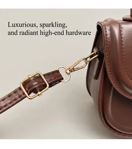 Detail of glossy gold metal hardware and brown leather stitching on a saddle bag