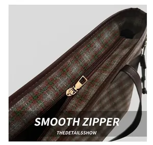 Detail of smooth gold metal zipper on a checkered tweed tote bag with leather piping