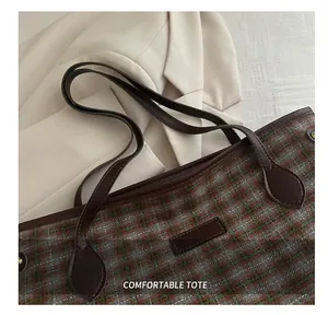 Detail of plaid tote bag showing brown leather straps and green checked fabric