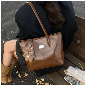 Brown leather tote bag detail with a cute plush bear pendant in an autumn outdoor setting