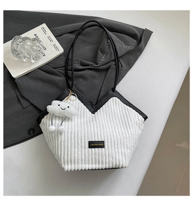 Close-up of white corduroy tote bag featuring black contrast leather trim and a smiley charm