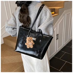 Side view of black glossy tote bag with teddy bear charm on casual indoor stairs
