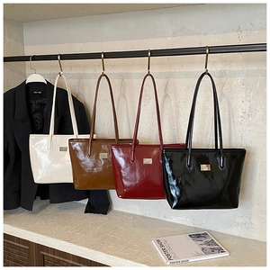 Fila de cuatro bolsos tote brillantes en crema, marrón, granate y negro sobre ganchos