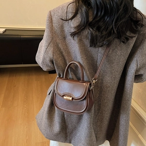 Retro dark brown saddle handbag with gold metal clasp on a model in a wool suit