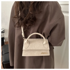 Close-up of a beige mini suede handbag with elegant top handle and gold logo detail