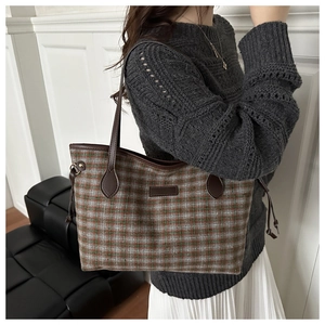 Detail view of large plaid tote bag featuring leather handles and side drawstring