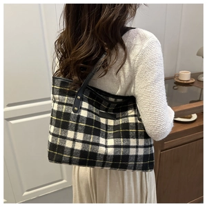 Detail of checkered tote bag with black leather handles and gold rivet accents