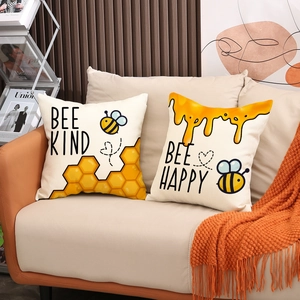 Dettaglio di cuscini in lino a tema ape con stampe Bee Kind e Bee Happy su divano