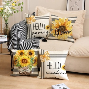 Detail of four sunflower linen pillow covers with hello spring text on a beige sofa