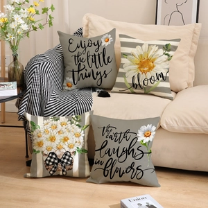 Detail of four linen pillow covers with daisy prints and motivational quotes on a sofa