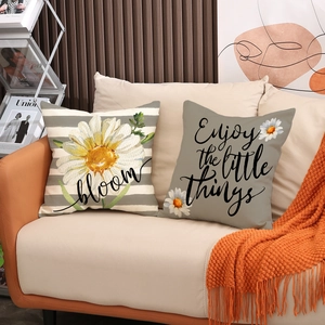 Close-up of minimalist linen pillow covers with daisy prints and motivational quotes on a sofa