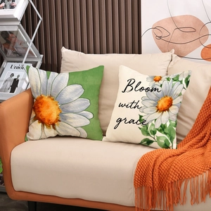 Close-up of daisy print cushion covers with Bloom with grace text on a beige sofa