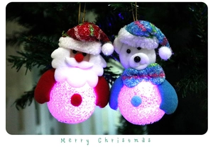 Close-up of hanging LED Santa and bear ornaments with pink light on Christmas tree branch