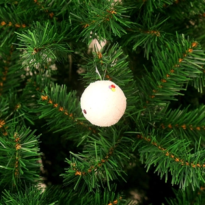 Close-up of white snow-textured Christmas ball with sequins hanging on a green tree branch