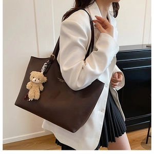 Macro detail of dark brown leather tote bag featuring a cute plush bear charm accessory