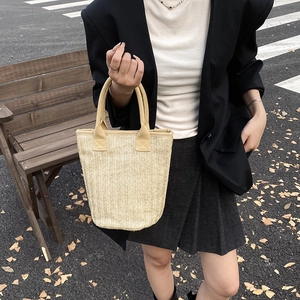 Beige woven bucket handbag with herringbone pattern shown in an outdoor autumn street setting