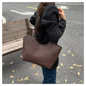 Detail of a large dark brown woven tote bag worn by a model in a casual outdoor setting