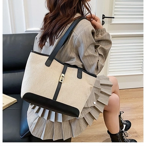 Détail du cabas contrasté en toile beige avec bordure en cuir noir et fermoir doré rotatif