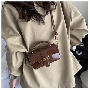 Sac bandoulière en cuir marron avec boucle dorée porté sur une tenue neutre