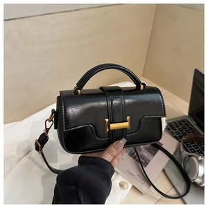 Close-up of black leather handbag featuring a gold square buckle and adjustable strap