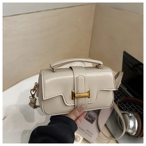 Close-up of cream leather crossbody bag featuring a golden H-buckle and top handle