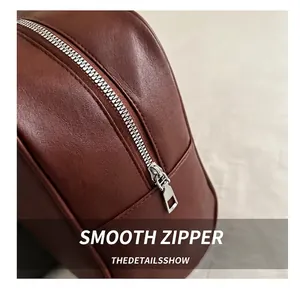 Close-up of smooth silver metal zipper and brown leather texture on a tote bag