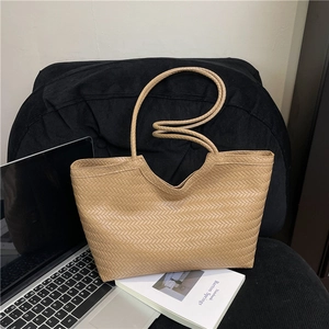 Borsa tote intrecciata color kaki con motivo a spina di pesce su sedia in velluto