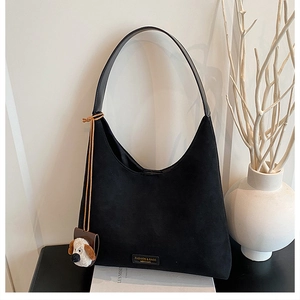 Détail d'un sac hobo en daim noir avec bandoulière en cuir et charm peluche chien