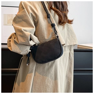 Détail du sac bandoulière noir mat avec bandoulière nouée et pendentif métallique