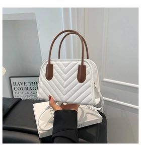 Close-up of white quilted handbag with brown round handle and V-shaped stitching detail