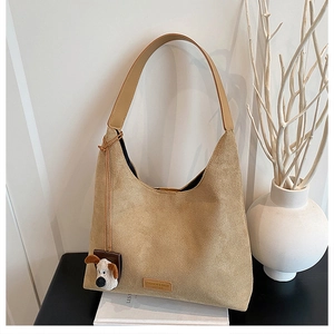 Détail macro du sac hobo en daim kaki avec étiquette en cuir et breloque peluche