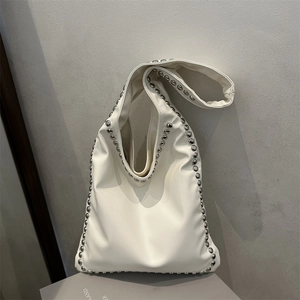 Minimalist beige shoulder bag with silver metallic studs and wide strap on geometric stand